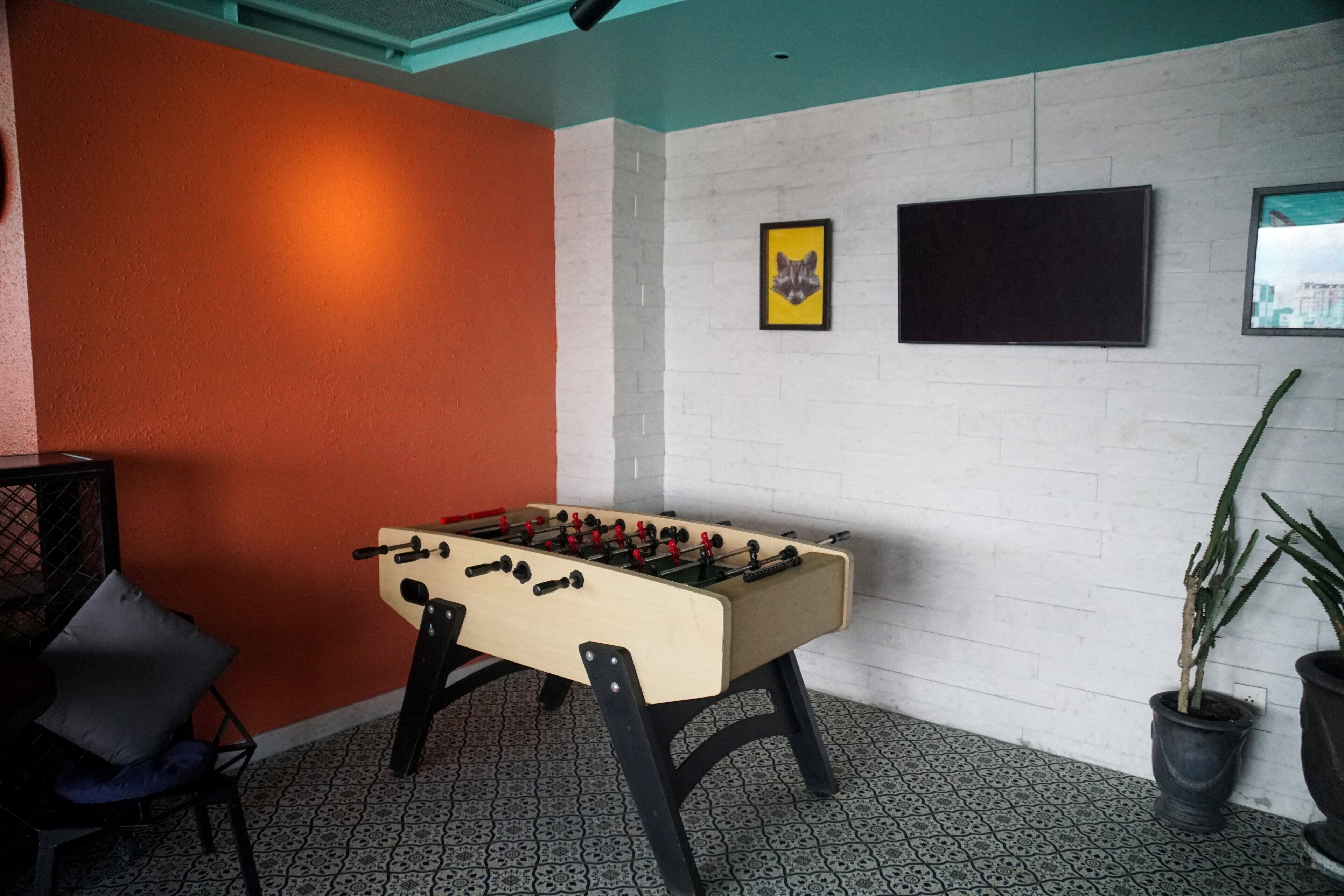 A room with a foosball table, a TV mounted on the wall, and a potted plant.