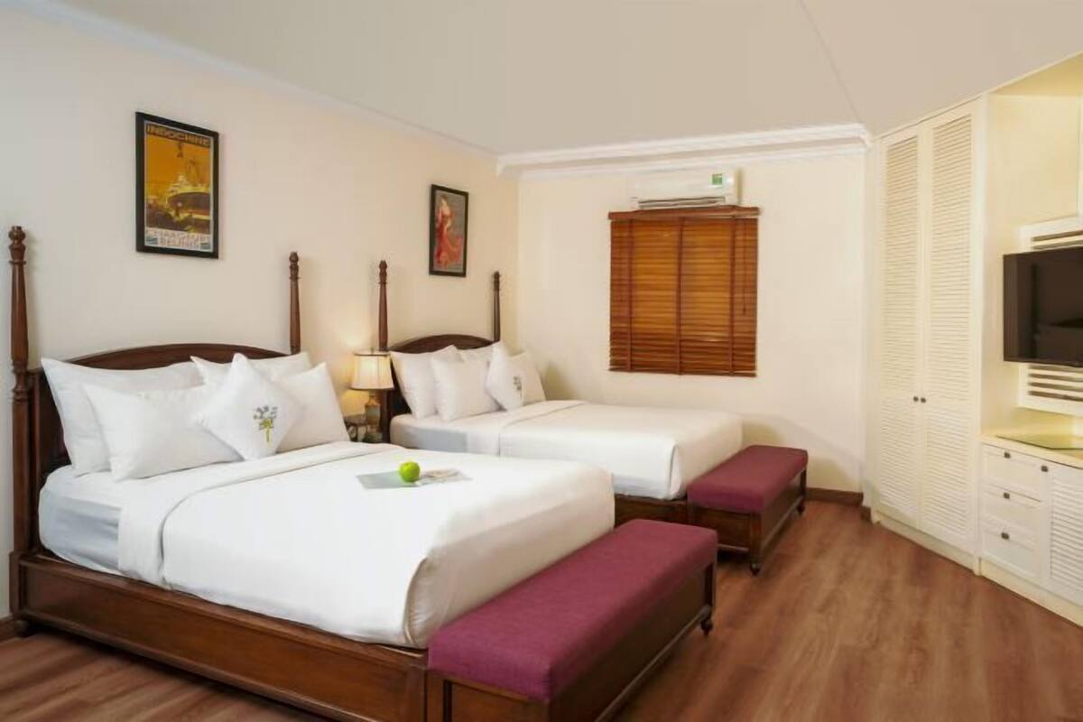 A hotel room with two beds, a TV, a wardrobe, and a window with blinds.
