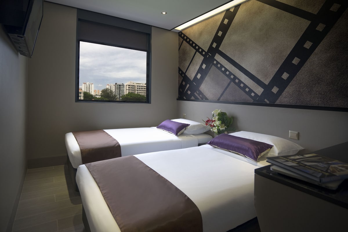 A hotel room with two beds, a large window, and a wall-mounted film strip artwork.