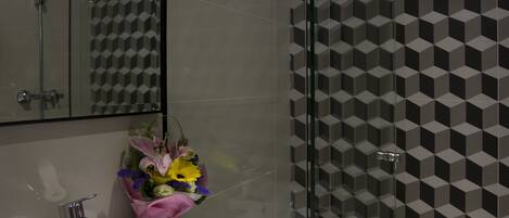 A modern bathroom with a glass shower enclosure, a white sink, and a decorative flower arrangement.