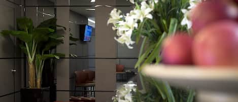 Un vestíbulo moderno con una planta grande en maceta, una zona de estar con sillas naranjas y un televisor de pantalla plana montado en la pared.