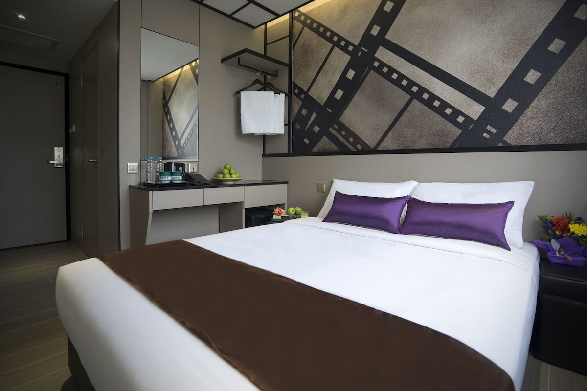 A hotel room with a large bed, a bedside table with a lamp, a mirror, and a wall art piece.