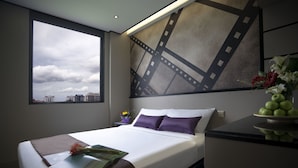 Quarto de hotel moderno com uma cama grande, vista do horizonte urbano por uma janela e uma obra de arte com tema de faixa de filme decorativa.