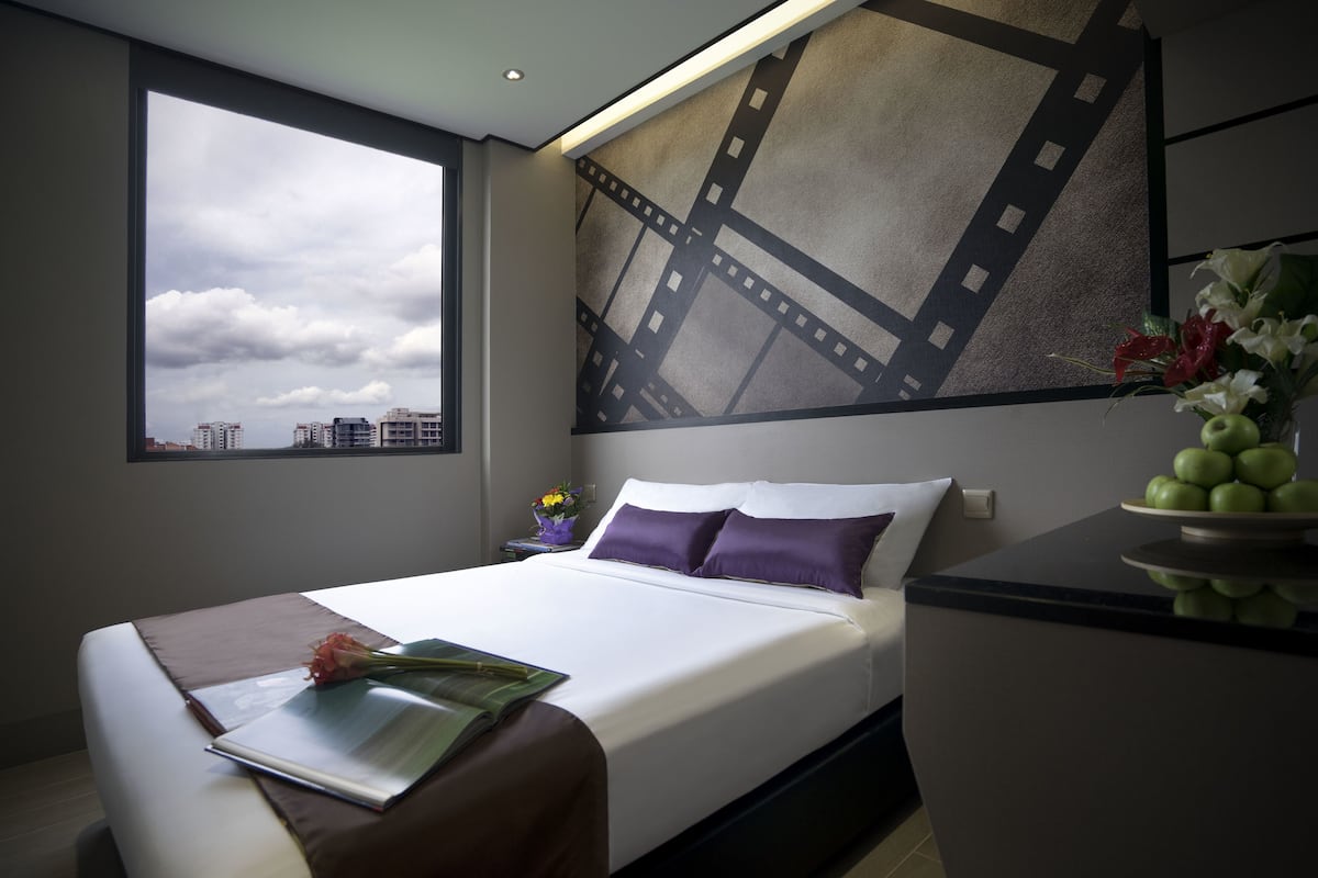A modern hotel room with a large bed, a view of the cityscape through a window, and a decorative film strip wall art piece.
