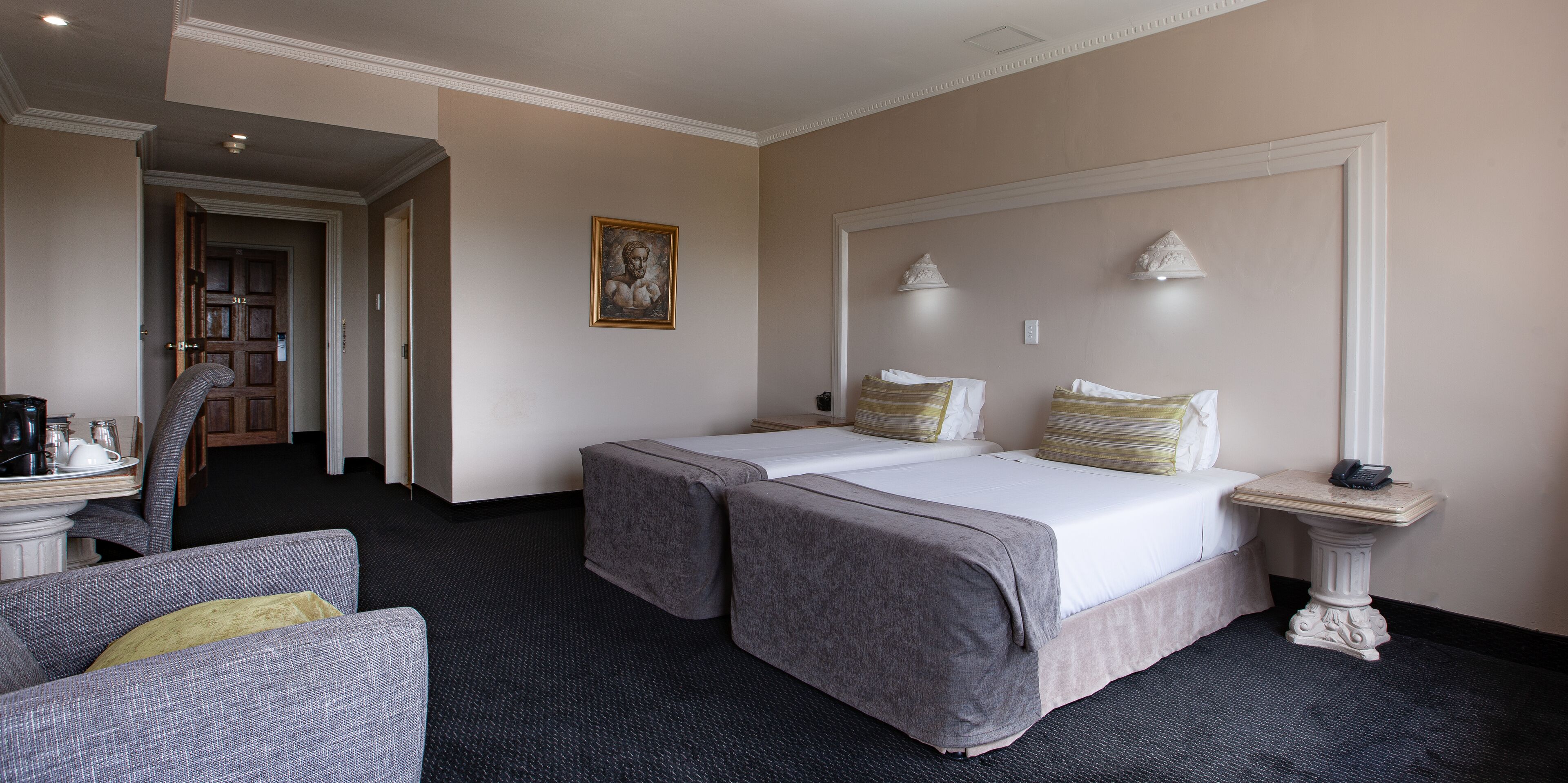 Habitación de hotel con dos camas, una mesita con un teléfono, una silla y un cuadro en la pared.