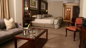 A hotel room with a bed, a sofa, a coffee table, and a chair. - Apollo Hotel (Randburg)
