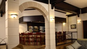 A bar area with a counter and stools, a seating area with a patterned sofa, and a dining setup with chairs and a table. - Apollo Hotel (Randburg)