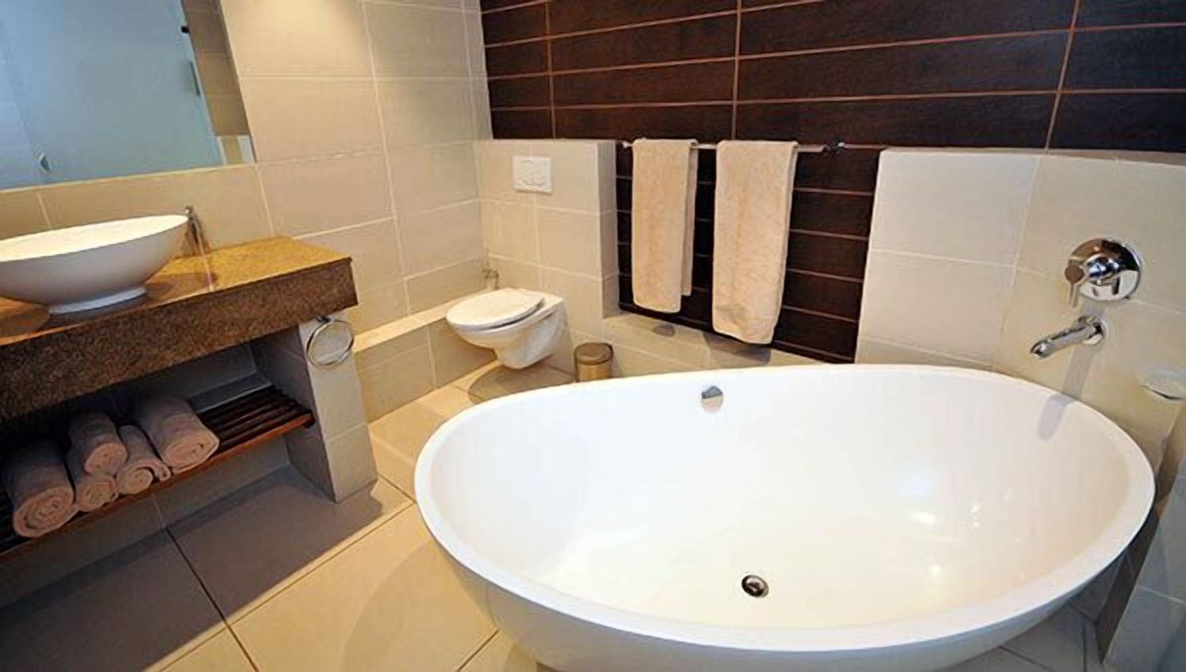 A modern bathroom with a large freestanding bathtub, a toilet, a sink, and towels on a shelf.