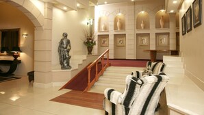 A grand lobby with a marble staircase, a statue, and framed portraits on the walls. - Apollo Hotel (Randburg)