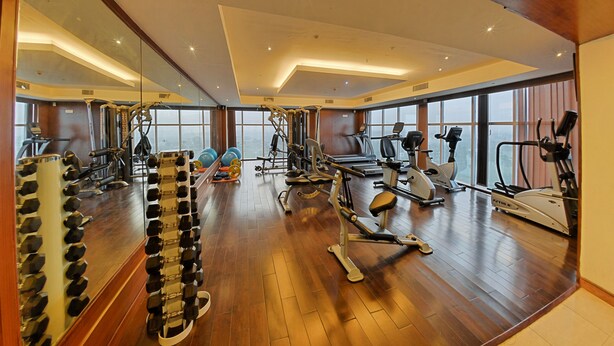 Un gimnasio amplio con diversos equipos de ejercicio, ventanas grandes y suelo de madera.
