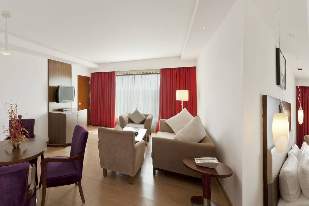 A hotel room with a bed, a desk, a chair, a sofa, and a TV.