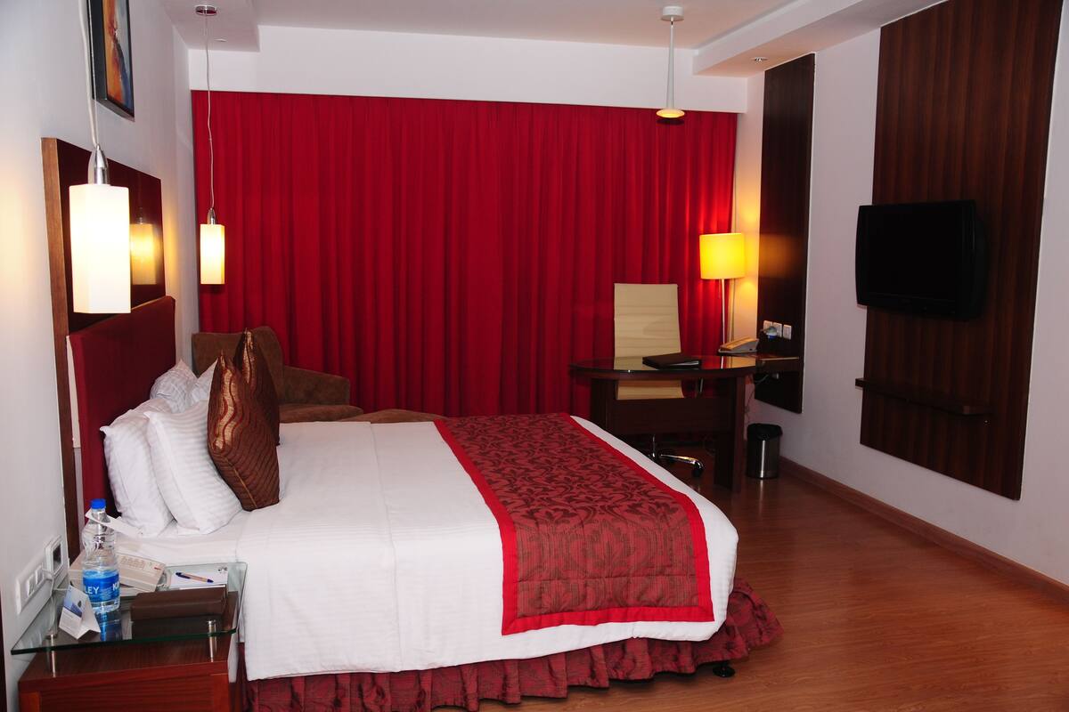 A hotel room with a large bed, a desk, a chair, a television, and a red curtain.