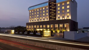 Un hotel moderno con una entrada destacada, varios pisos y ventanas iluminadas.