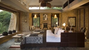 A spacious bedroom with a large bed, a stone fireplace, and a view of the outdoors. - Pashan Garh, Panna National Park (Panna)