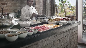 A chef preparing food in a kitchen with a brick wall, shelves with kitchenware, and a view of trees outside. - Pashan Garh, Panna National Park (Panna)