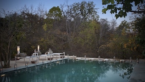 A serene outdoor pool area with a clear view of the water, surrounded by trees and furnished with a lounge chair and a small table. - Pashan Garh, Panna National Park (Panna)