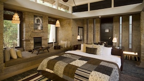 A spacious bedroom with a large bed, a stone fireplace, and a high ceiling fan. - Pashan Garh, Panna National Park (Panna)