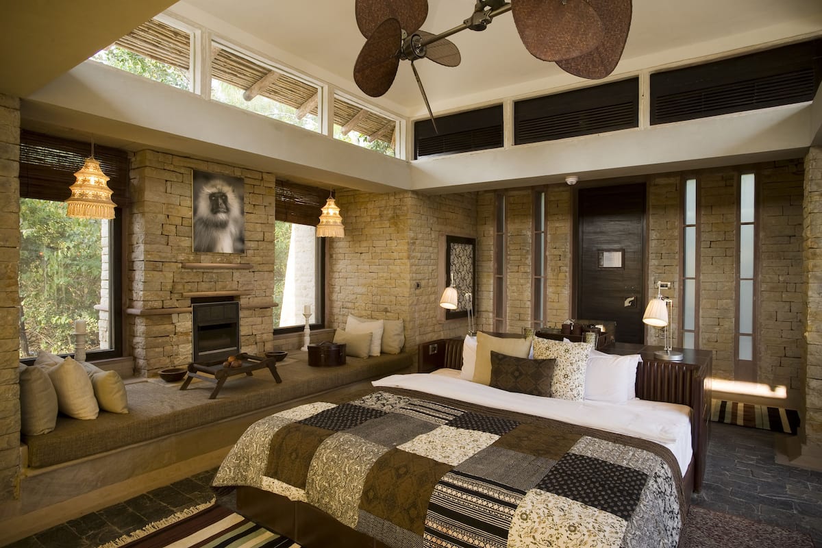 A spacious bedroom with a large bed, a stone fireplace, and a high ceiling fan.
