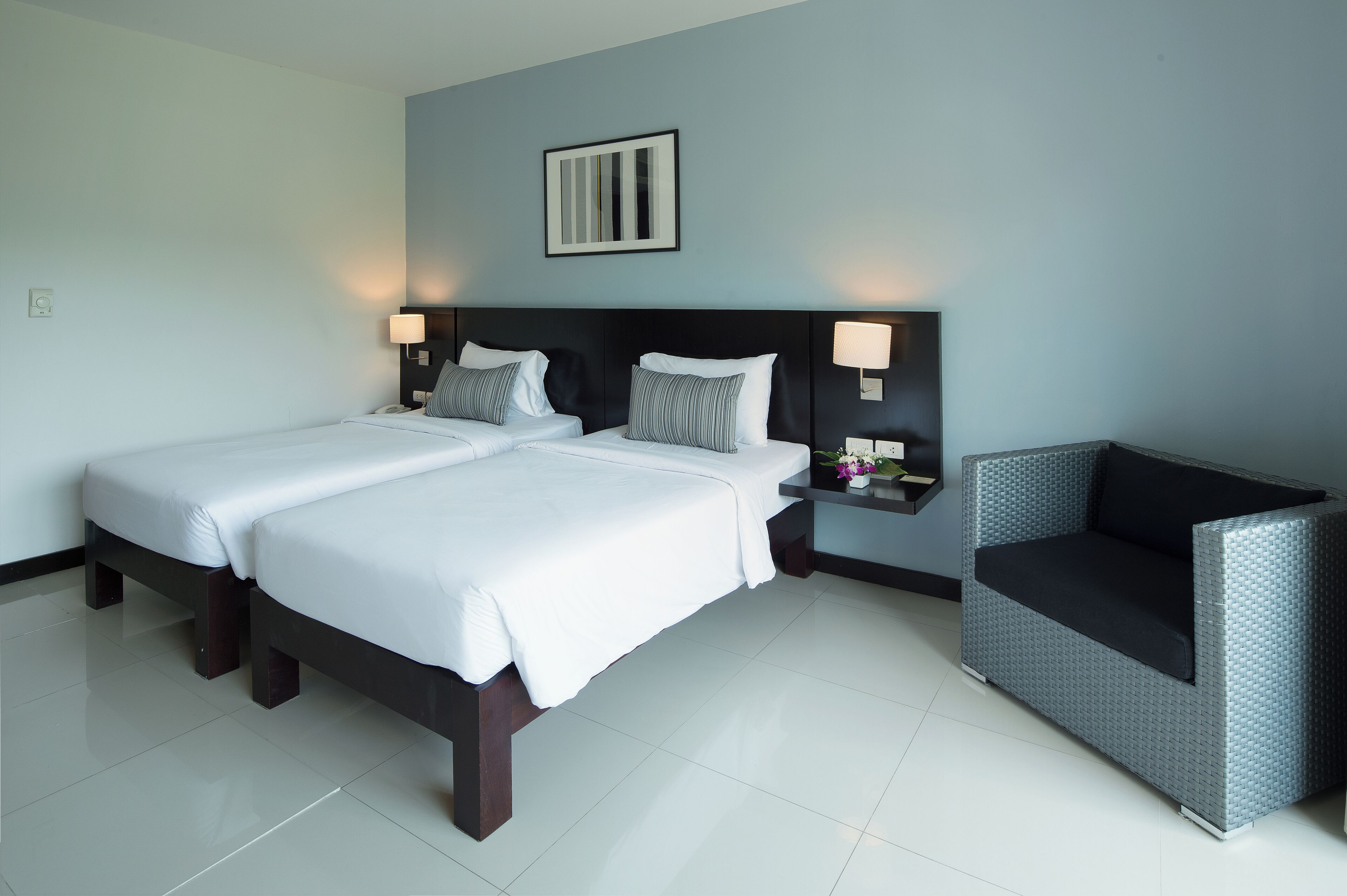 A hotel room with two beds, a nightstand, a chair, and a wall-mounted picture.