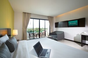 A hotel room with a bed, a laptop, a TV, a chair, and a balcony with a view.