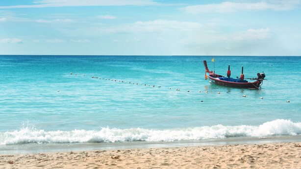 A boat anchored on a sandy beach with clear turquoise water. - Simplitel (Karon)
