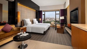 Ein Hotelzimmer mit Blick auf die Stadt, mit zwei Betten, einem Sofa, einem Fernseher und einem Essbereich.