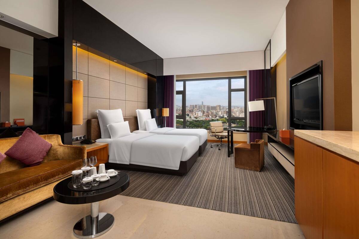 Habitación de hotel con vista a la ciudad, dos camas, un sofá, un televisor y un área de comedor.