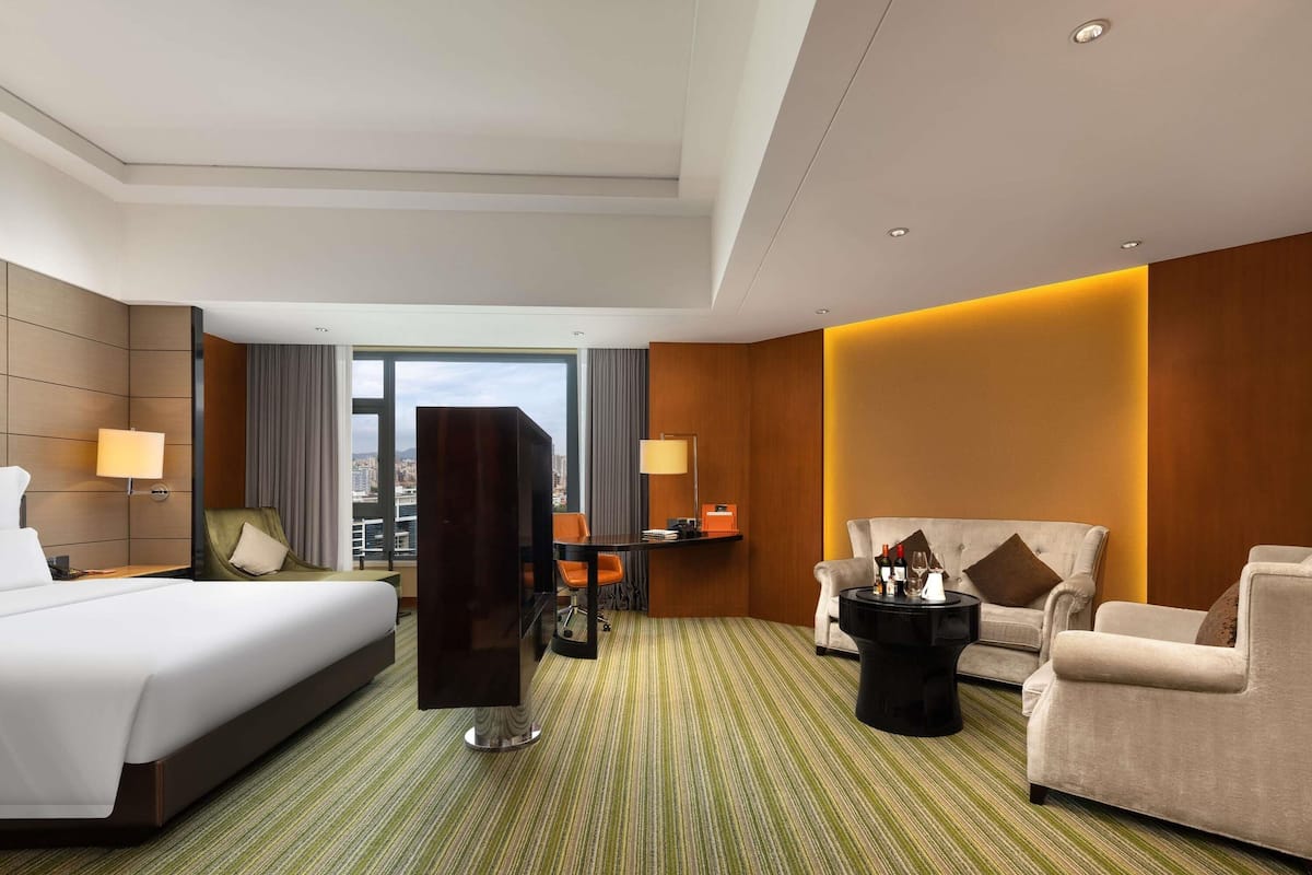Habitación de hotel con una cama grande, dos sillones, un sofá, una mesita y vistas a la ciudad.