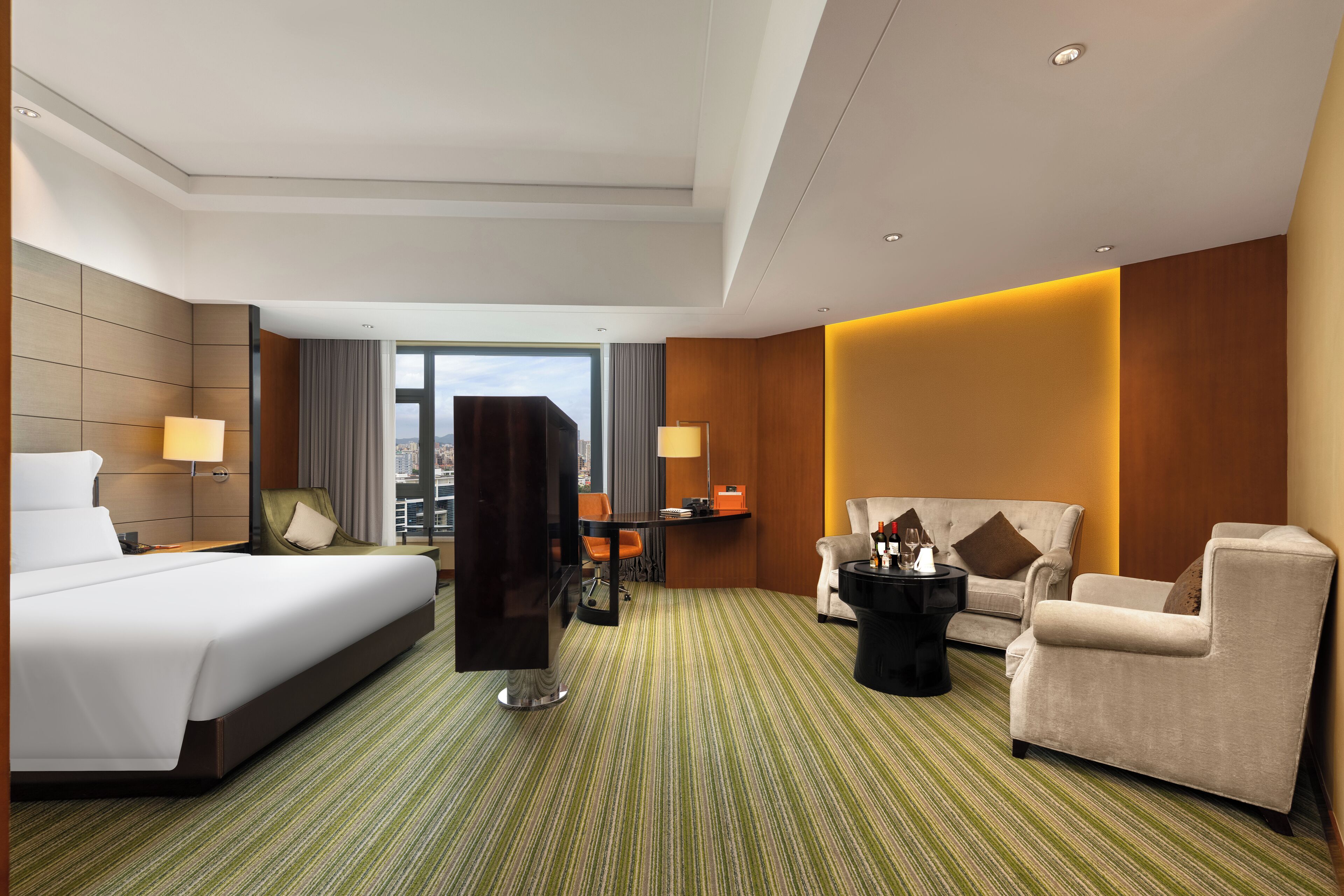 A hotel room with a large bed, two armchairs, a sofa, a desk, and a view of the city.