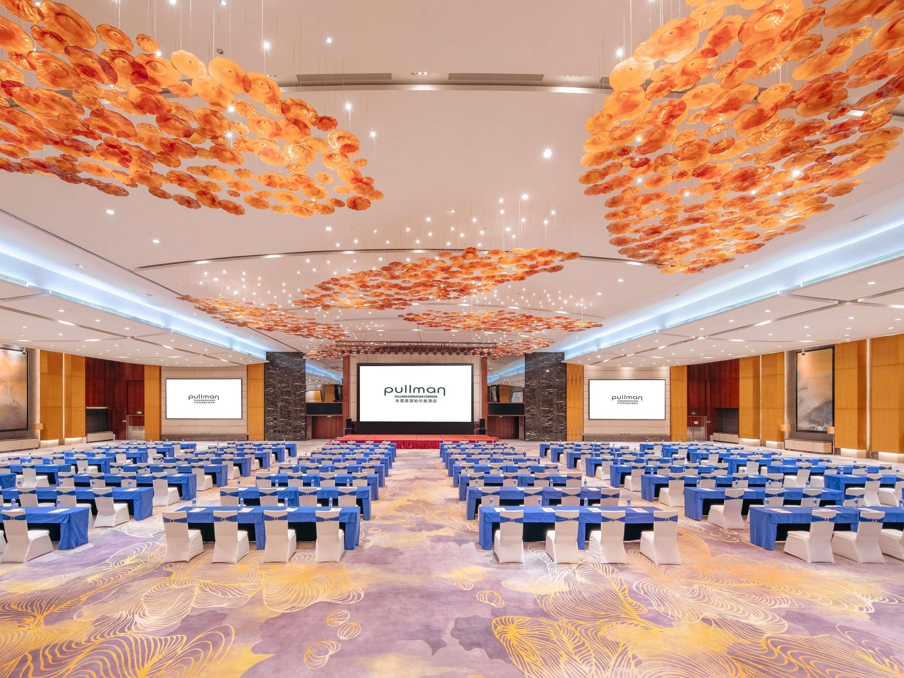 A conference room with rows of tables and chairs, a large screen, and a decorative ceiling.