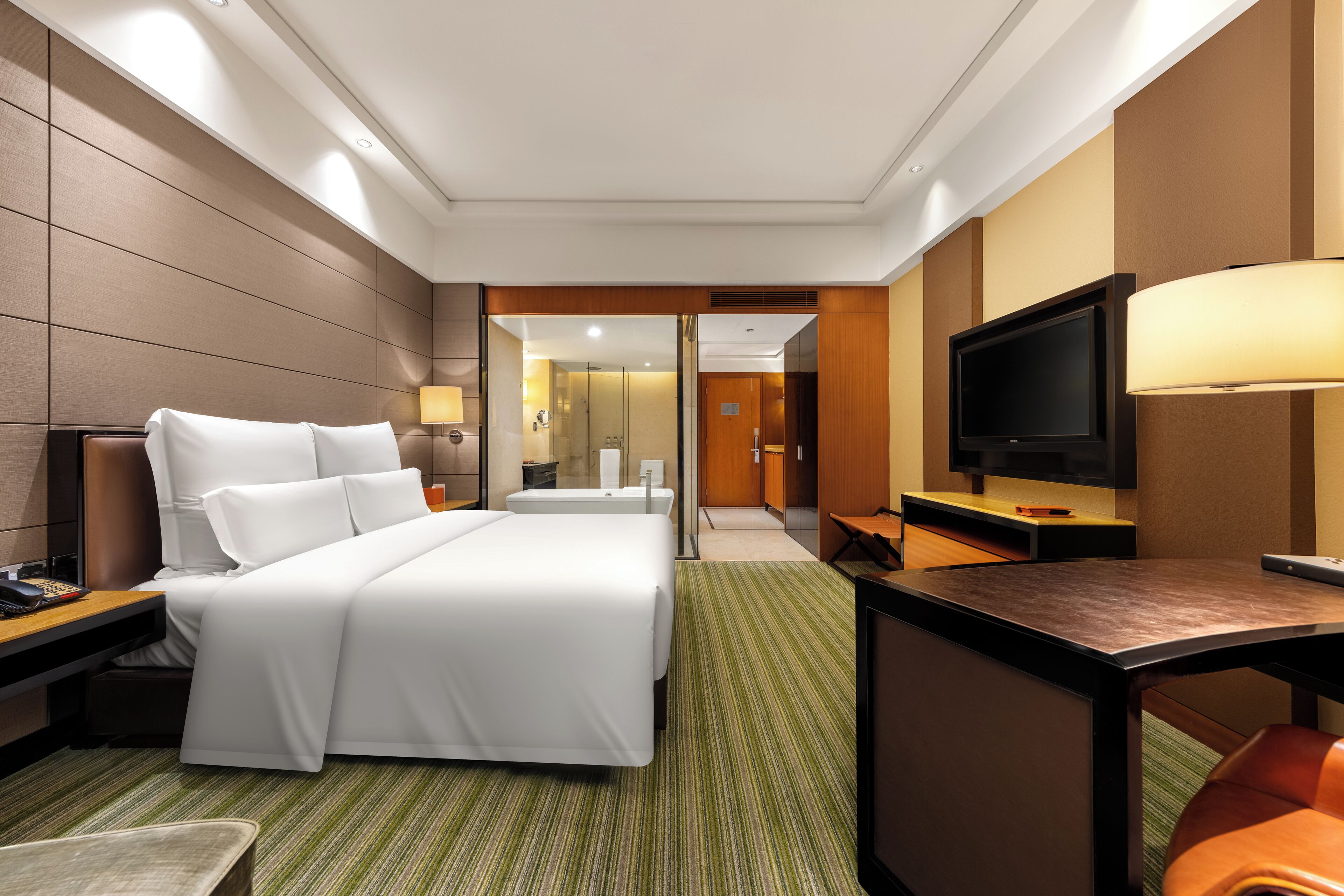 Habitación de hotel con una cama grande, televisión, escritorio y baño visible a través de una puerta abierta.