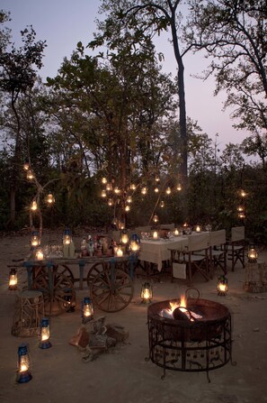 An outdoor dining setup with tables, chairs, lanterns, and a fire pit.