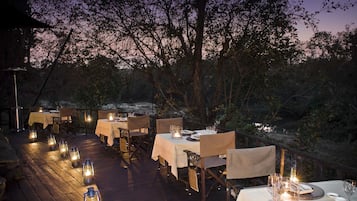 An outdoor dining area with tables and chairs, lanterns, and a view of the surrounding landscape.