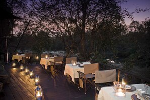 An outdoor dining area with tables and chairs, lanterns, and a view of the surrounding landscape.