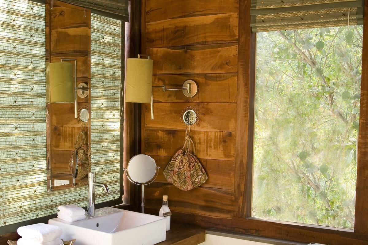 A wooden bathroom with a large window, a sink, a mirror, and a decorative chest.