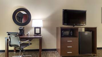 A hotel room with a desk, chair, television, microwave, and refrigerator.