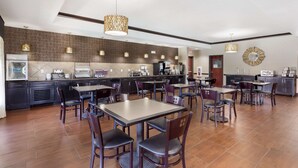 Un'ampia sala ristorante con numerosi tavoli e sedie, una zona cucina e lampade decorative.