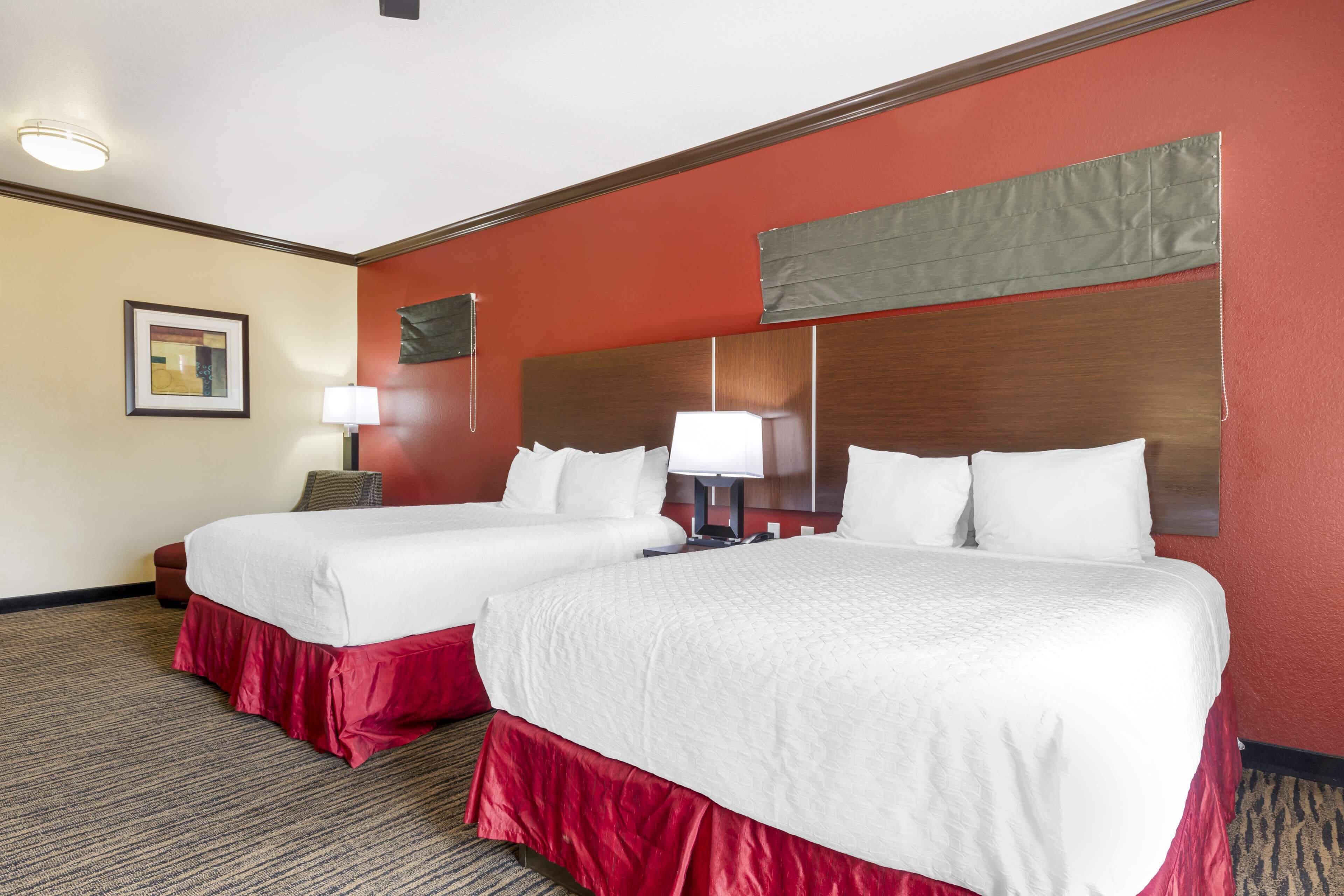 Quarto de hotel com duas camas, um tapete vermelho, um quadro na parede e um espelho sobre as camas.