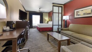Camera d'albergo con un letto, un divano, una scrivania con una sedia, una televisione e una lampada.