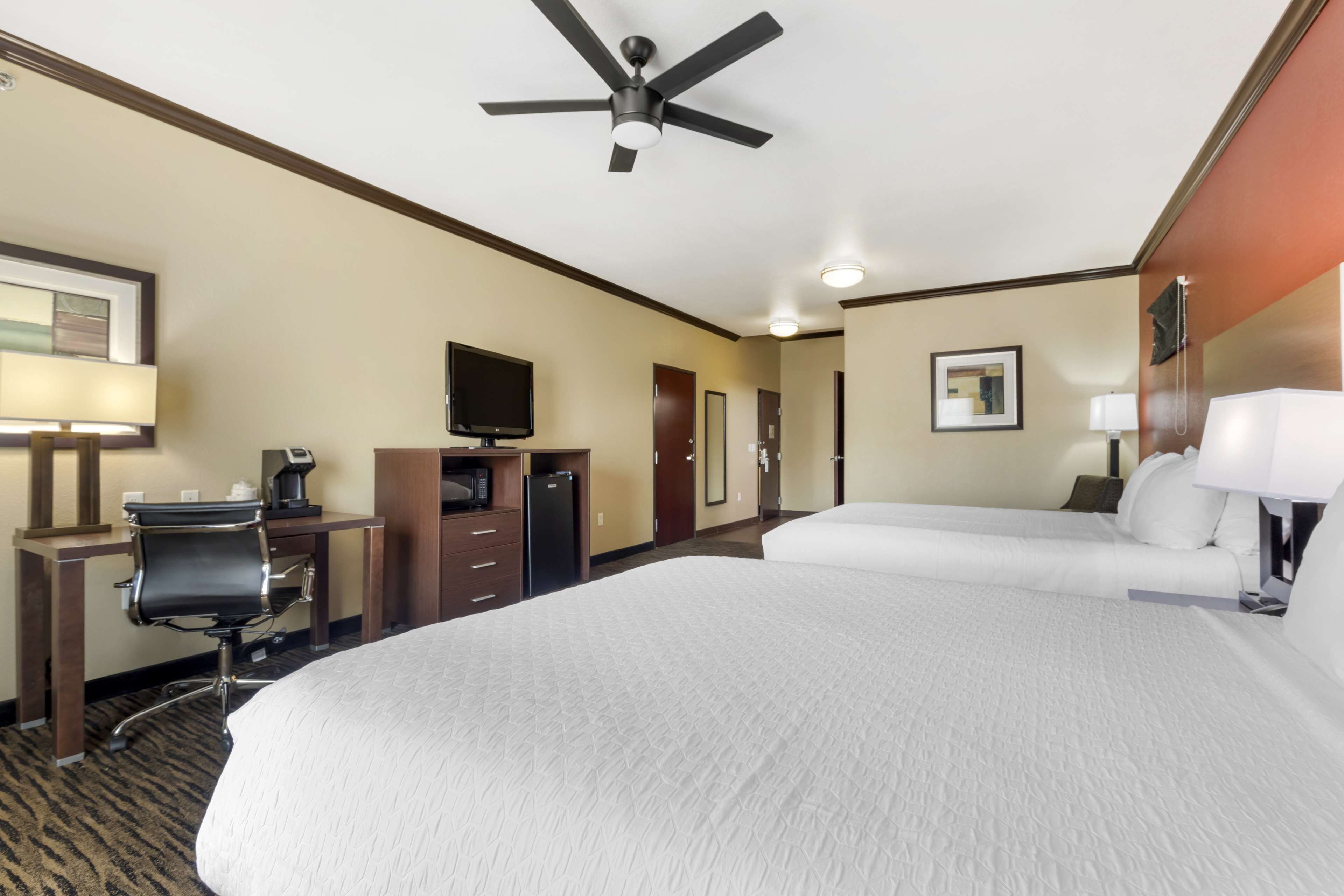 A hotel room with a large bed, a desk with a chair, a television, and a ceiling fan.