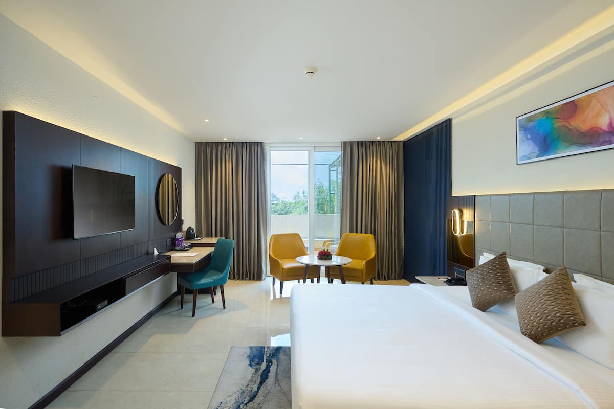 Una habitación de hotel moderna con una cama grande, un escritorio con silla, un televisor de pantalla plana y un ventanal con cortinas.