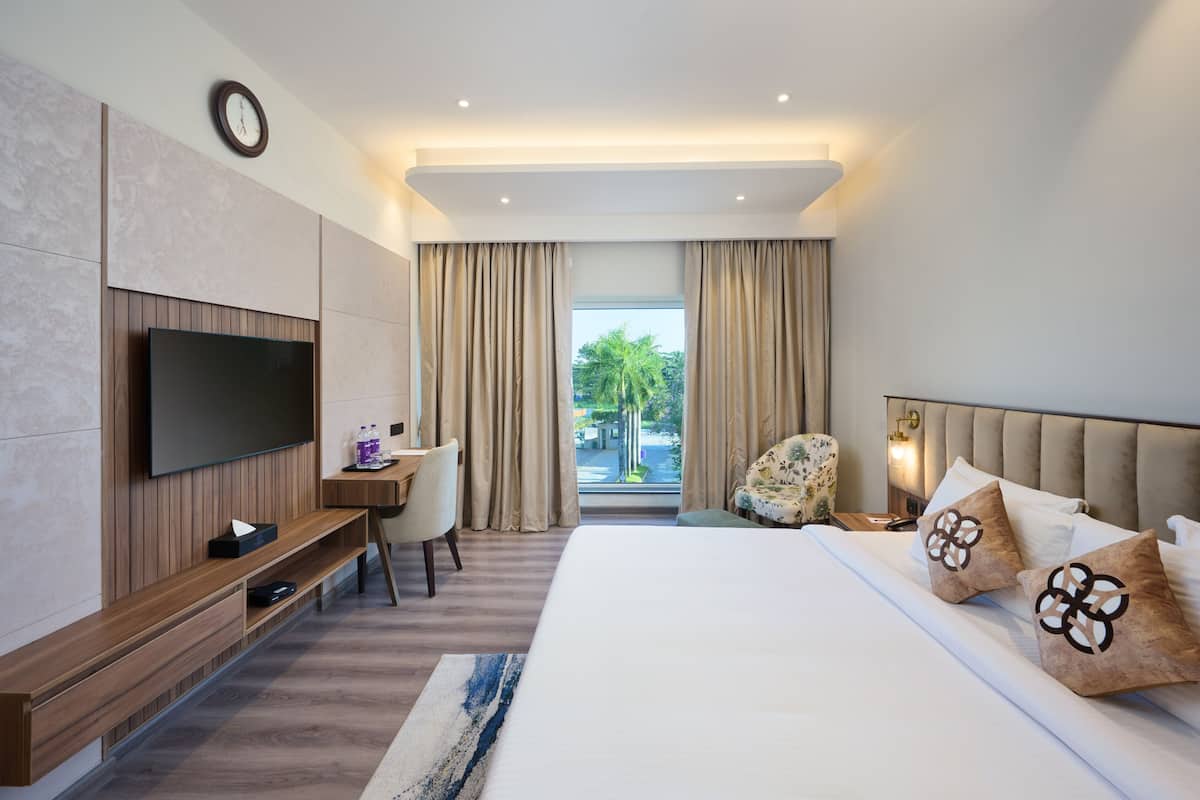 Habitación de hotel moderna con una cama grande, un televisor de pantalla plana, un escritorio y vistas a palmeras a través de la ventana.