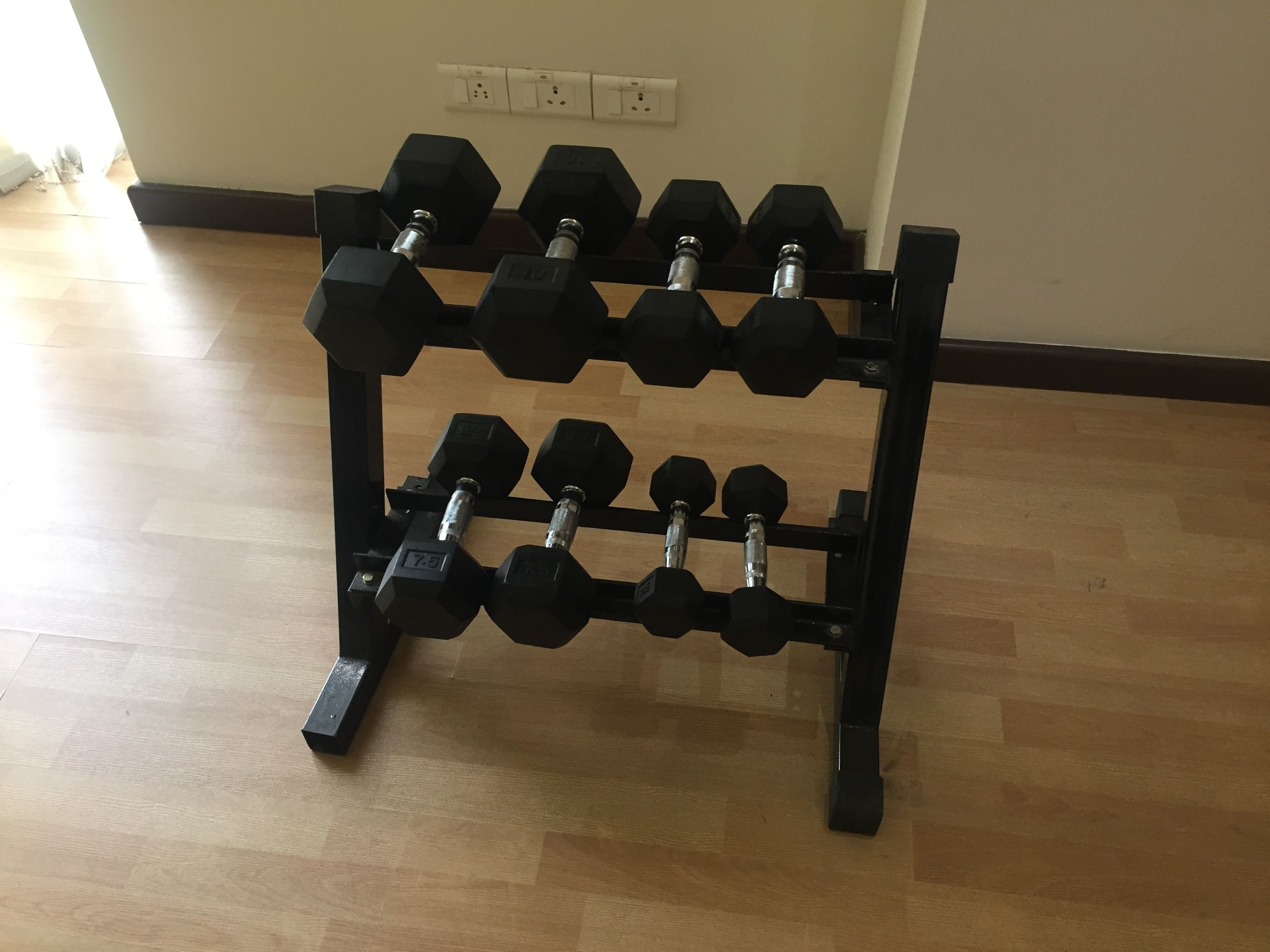 A black dumbbell rack with multiple pairs of hexagonal dumbbells on a wooden floor.
