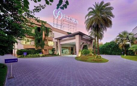 A hotel entrance with a sign reading "FLORA," a covered walkway, and a landscaped area with palm trees.