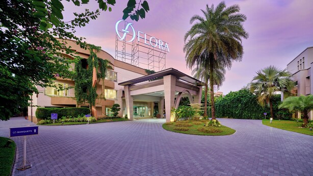 A hotel entrance with a sign reading "FLORA," a covered walkway, and a landscaped area with palm trees.