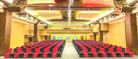 Un salón amplio con filas de sillas y un escenario.