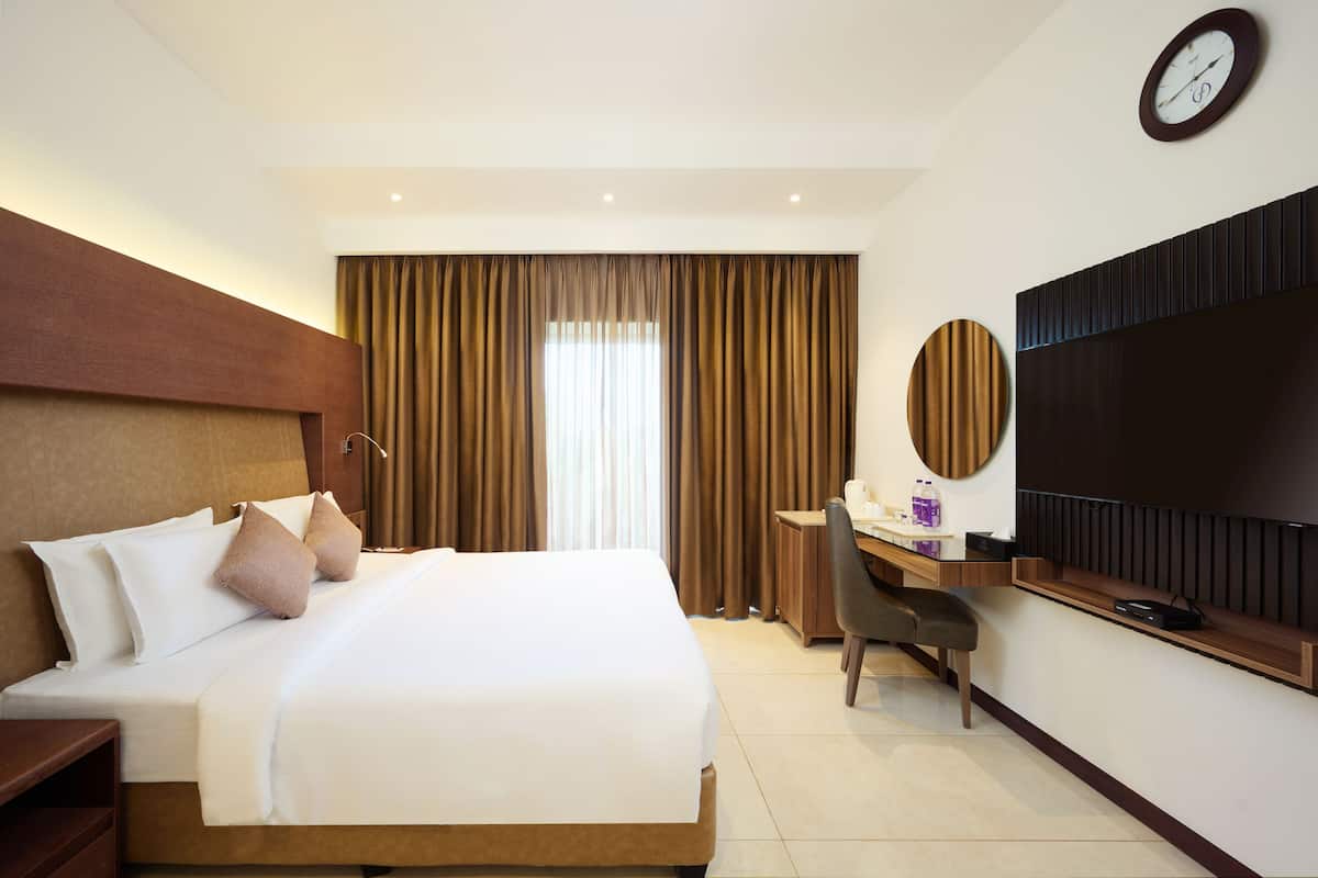 Una habitación de hotel con una cama grande, un escritorio, una silla, un televisor y una ventana con cortinas.