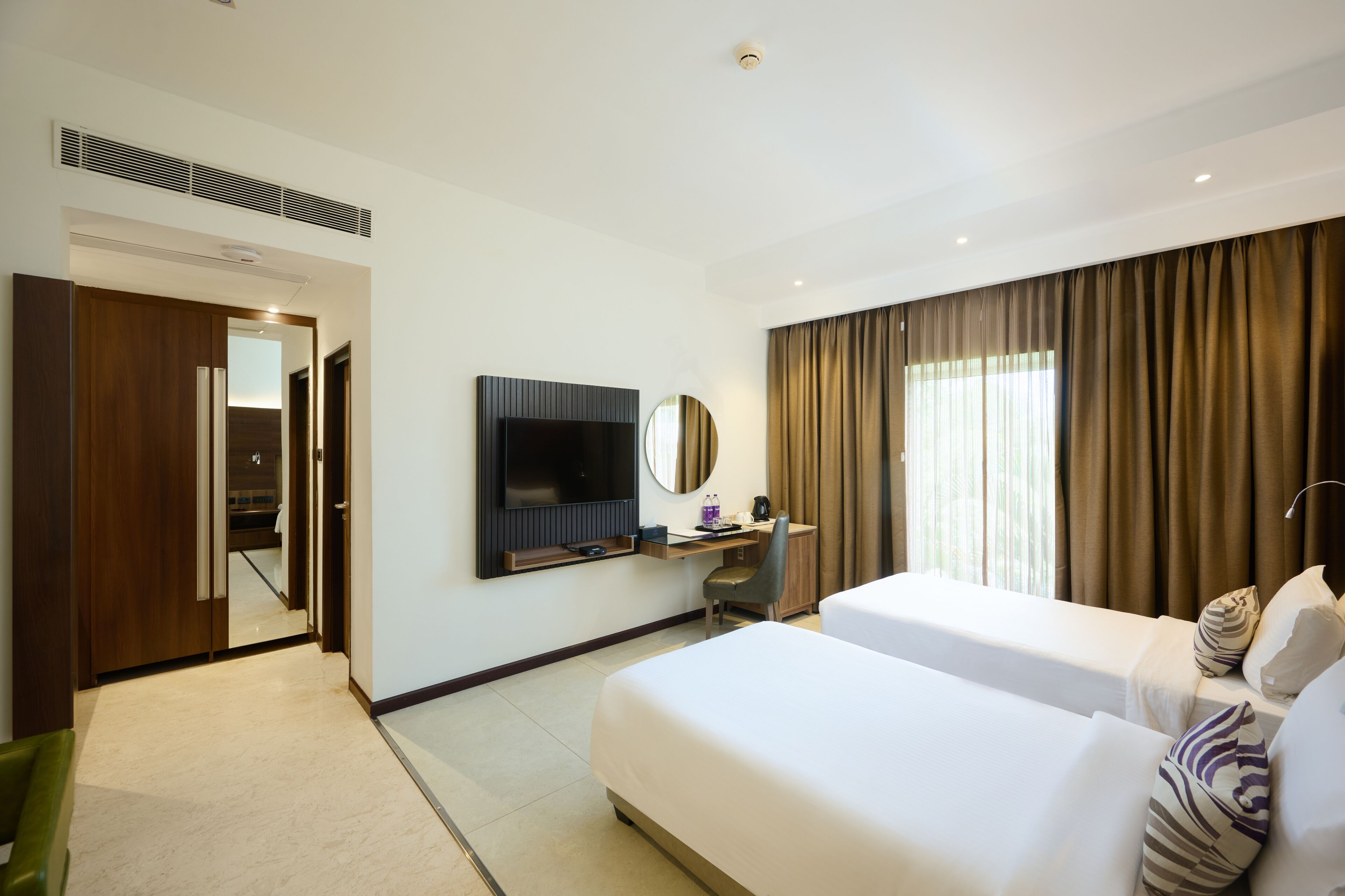 A hotel room with two beds, a desk, a TV, and a mirror.
