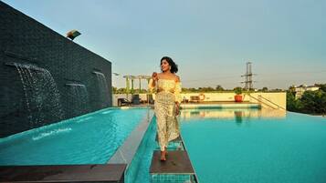 A person standing on a poolside platform with a clear view of a swimming pool and a building with a water feature.