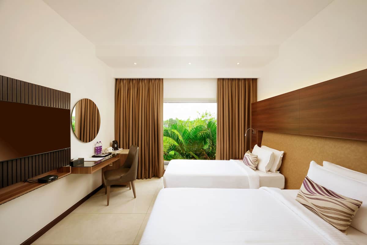 Habitación de hotel con dos camas, un escritorio, una silla, un televisor y vistas a zonas verdes.